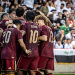 Soccer team celebrates together after scoring a goal in front of the crowd.