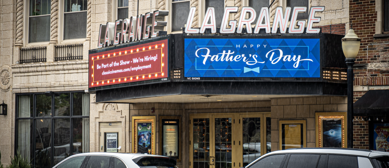Front entrance of the LaGrange Theater with a marquee displaying "Happy Father's Day" and a hiring announcement, with cars parked along the street.