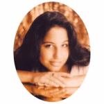 Portrait of a Lisa with long dark hair, smiling while resting her chin on her folded arms.