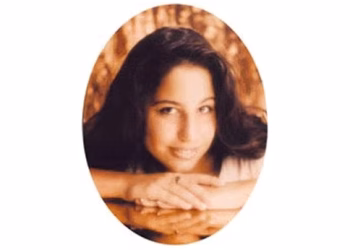 Portrait of a Lisa with long dark hair, smiling while resting her chin on her folded arms.