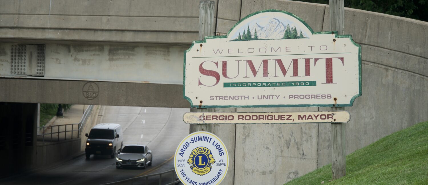 Welcome sign for the Village of Summit beside a road leading under an overpass.