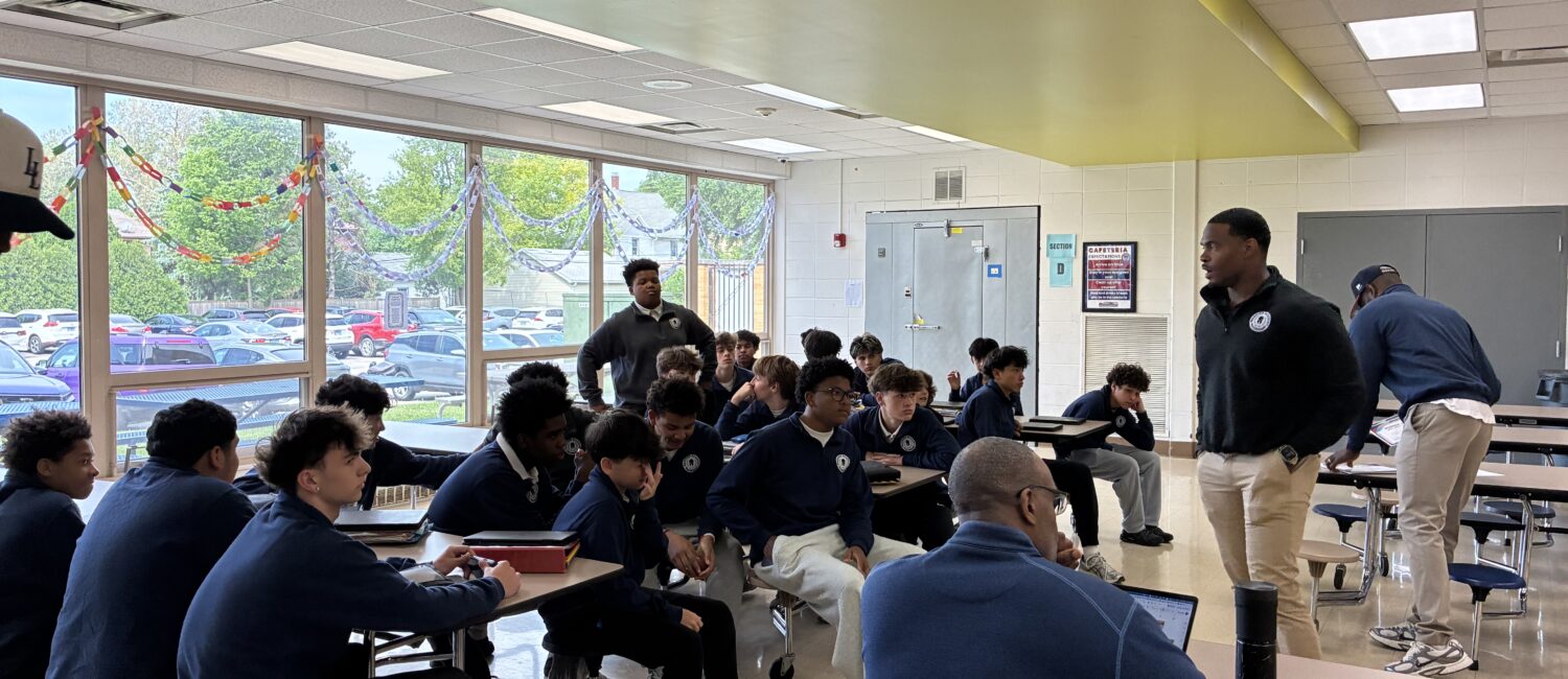 Students in a school cafeteria listen as staff members lead a group discussion during a session of the men's mental health warrior academy during school.