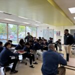 Students in a school cafeteria listen as staff members lead a group discussion during a session of the men's mental health warrior academy during school.
