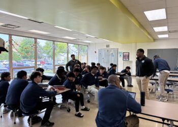 Students in a school cafeteria listen as staff members lead a group discussion during a session of the men's mental health warrior academy during school.